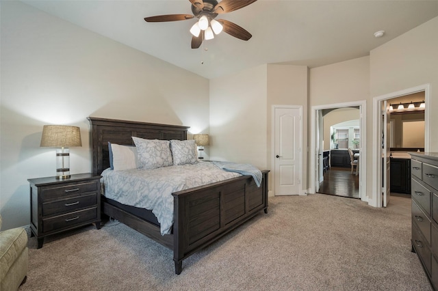 bedroom featuring arched walkways, ceiling fan, light carpet, and ensuite bath