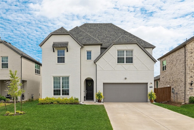 french country style house with driveway, brick siding, a front lawn, an attached garage, and a shingled roof