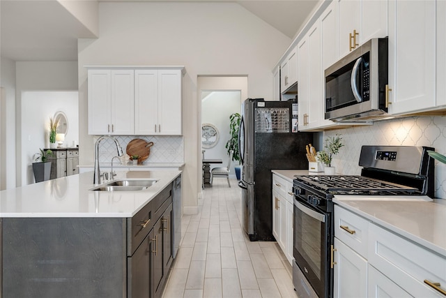 kitchen with a sink, light countertops, an island with sink, stainless steel appliances, and tasteful backsplash