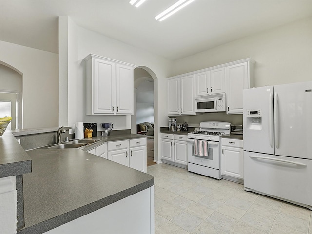 kitchen with arched walkways, a sink, dark countertops, and white appliances