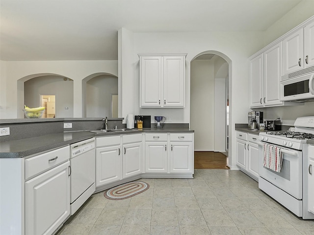 kitchen featuring dark countertops, a sink, white appliances, arched walkways, and white cabinetry