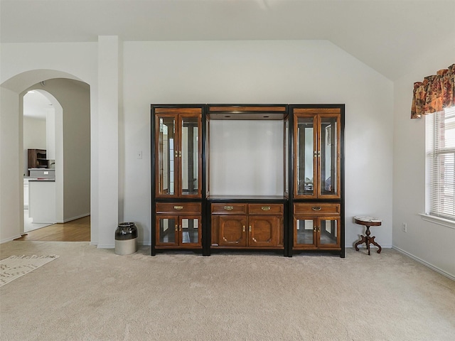 living area with arched walkways, baseboards, light colored carpet, and vaulted ceiling