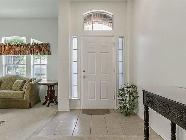 entryway featuring light tile patterned floors, baseboards, light carpet, and a towering ceiling