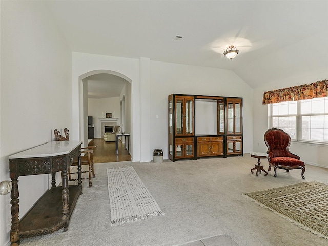 sitting room featuring visible vents, lofted ceiling, carpet flooring, a fireplace, and arched walkways