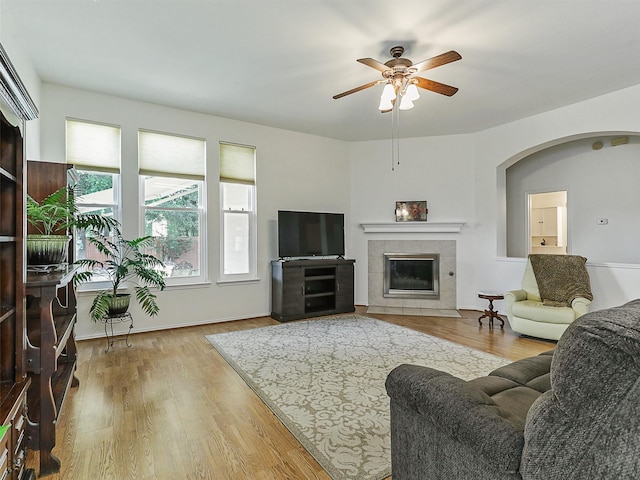 living area featuring a tiled fireplace, arched walkways, ceiling fan, and wood finished floors