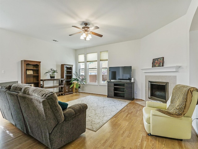 living room with a tiled fireplace, ceiling fan, wood finished floors, and visible vents
