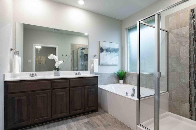 bathroom with double vanity, a bath, a stall shower, wood finished floors, and a sink