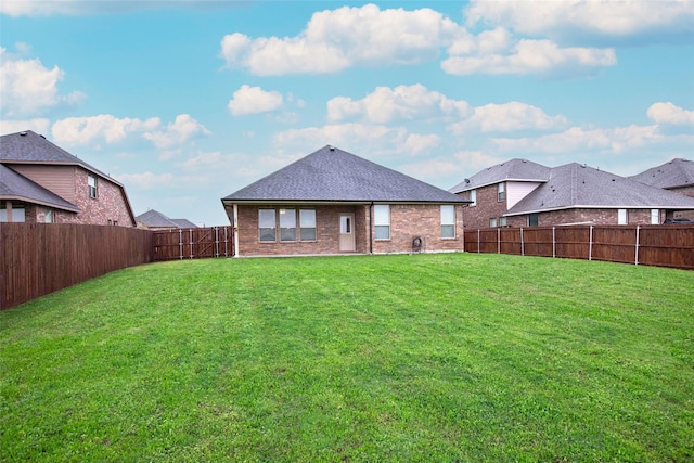 back of property featuring brick siding, a fenced backyard, a yard, and a shingled roof