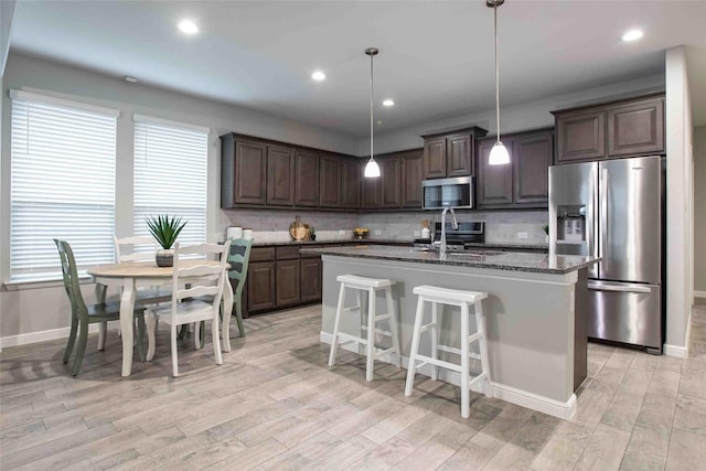 kitchen featuring dark brown cabinetry, backsplash, light wood-type flooring, a sink, and stainless steel appliances