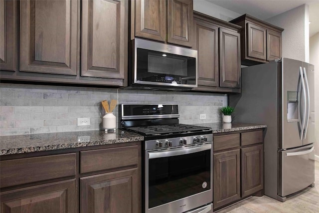 kitchen with decorative backsplash, dark brown cabinetry, light wood-type flooring, dark stone counters, and stainless steel appliances