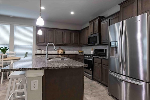 kitchen featuring decorative backsplash, dark brown cabinetry, appliances with stainless steel finishes, a sink, and dark stone countertops