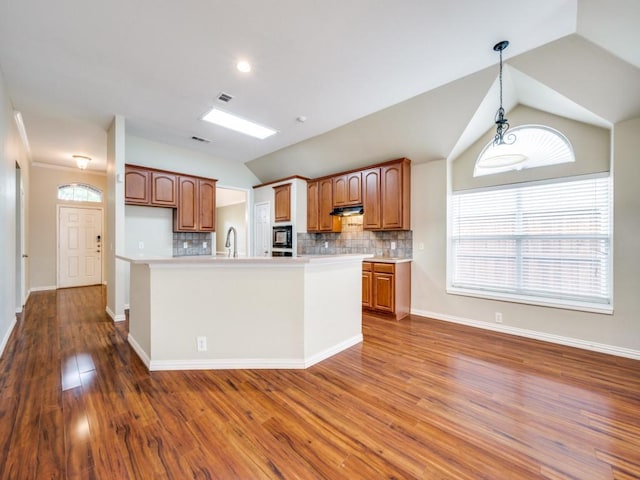 kitchen with black microwave, decorative backsplash, wood finished floors, and lofted ceiling