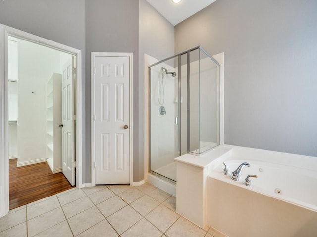 bathroom featuring tile patterned floors, baseboards, a bath, and a stall shower