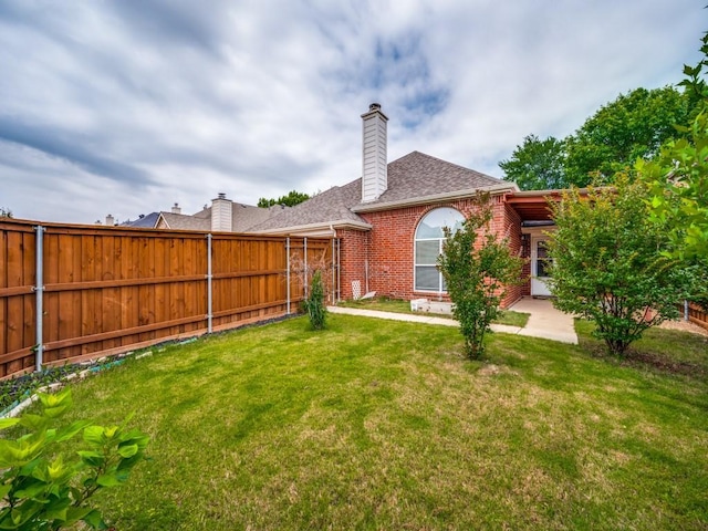 back of property featuring fence, a chimney, a lawn, and brick siding