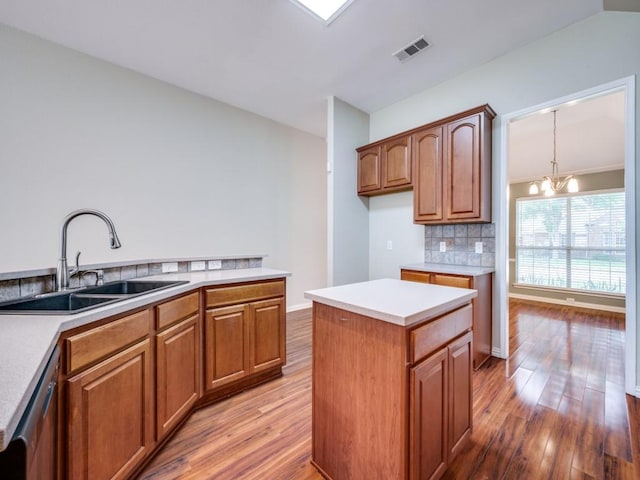 kitchen featuring visible vents, decorative backsplash, a sink, light wood finished floors, and a notable chandelier