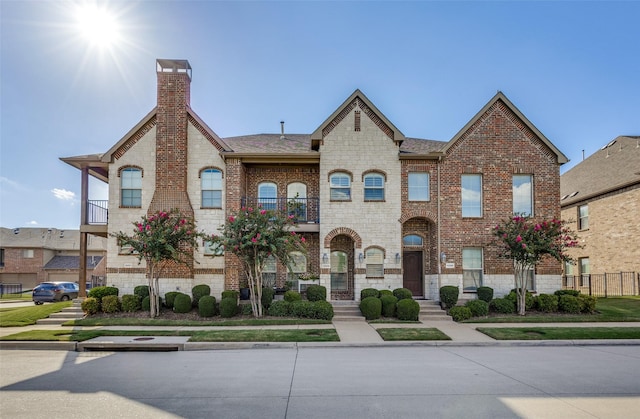 multi unit property featuring brick siding, roof with shingles, a chimney, and stone siding