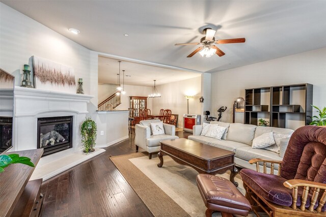 living area featuring a glass covered fireplace, ceiling fan with notable chandelier, recessed lighting, baseboards, and dark wood-style floors