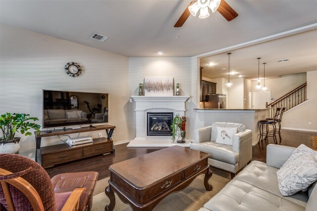 living room with a ceiling fan, visible vents, wood finished floors, baseboards, and a glass covered fireplace