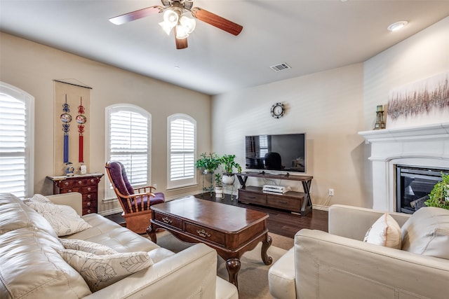 living area with visible vents, a glass covered fireplace, wood finished floors, baseboards, and a ceiling fan