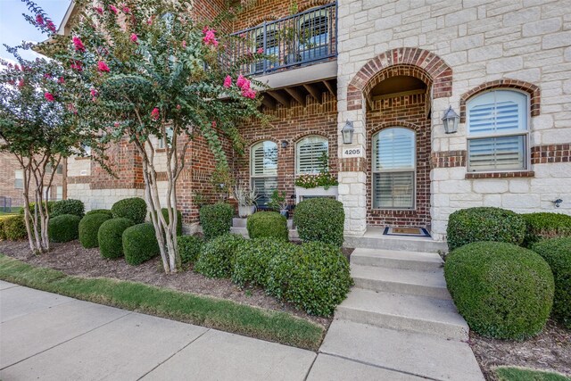 doorway to property with brick siding, a balcony, and stone siding