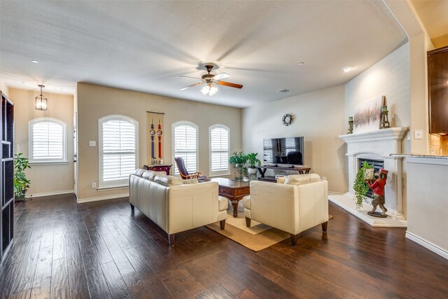 living area with ceiling fan, visible vents, dark wood finished floors, baseboards, and a fireplace with raised hearth