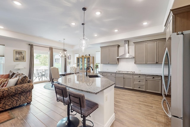 kitchen featuring a sink, a kitchen breakfast bar, wall chimney exhaust hood, stainless steel appliances, and open floor plan