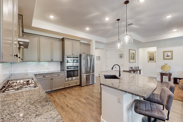 kitchen featuring appliances with stainless steel finishes, a sink, a raised ceiling, and a kitchen bar