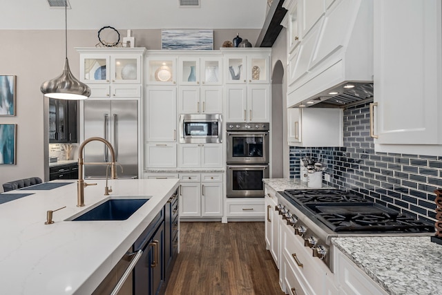kitchen featuring a sink, built in appliances, premium range hood, and white cabinets