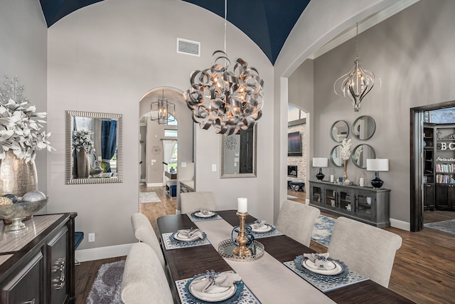 dining room featuring visible vents, a towering ceiling, wood finished floors, a chandelier, and arched walkways