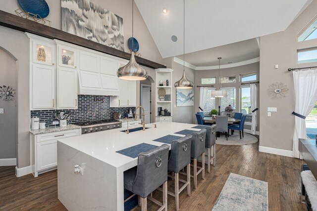 kitchen with baseboards, a sink, white cabinets, and high vaulted ceiling