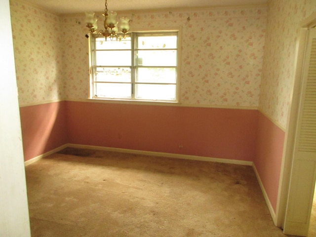 empty room featuring a wainscoted wall, wallpapered walls, and a notable chandelier