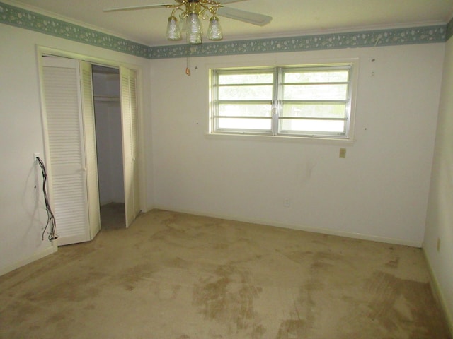 unfurnished bedroom featuring a closet, ornamental molding, baseboards, ceiling fan, and light colored carpet