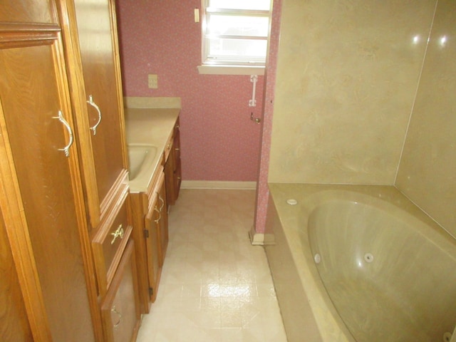 bathroom with baseboards, a tub with jets, wallpapered walls, and vanity