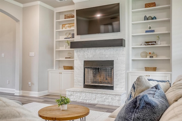 living area featuring ornamental molding, a brick fireplace, wood finished floors, baseboards, and arched walkways