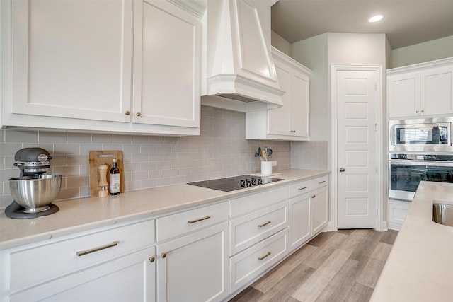 kitchen featuring white cabinetry, appliances with stainless steel finishes, custom range hood, and light wood-type flooring