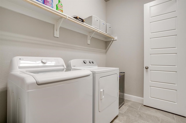 clothes washing area featuring washer and dryer, light tile patterned floors, laundry area, and baseboards