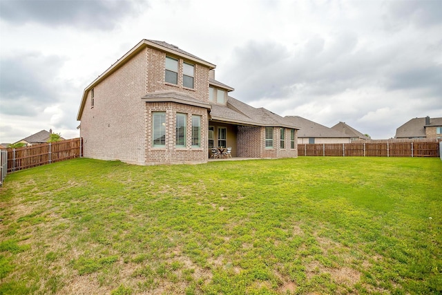 rear view of property with brick siding, a fenced backyard, and a lawn
