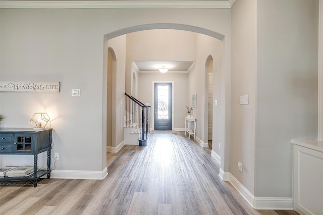 entrance foyer featuring crown molding, arched walkways, baseboards, wood finished floors, and stairway