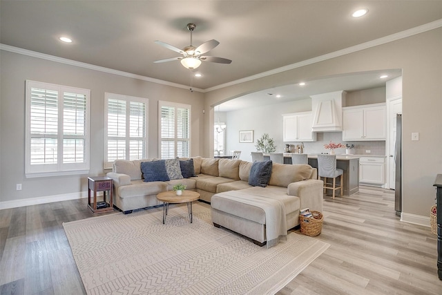living room featuring arched walkways, a ceiling fan, a wealth of natural light, and ornamental molding