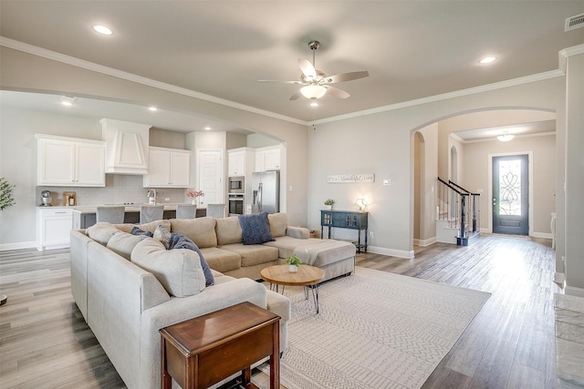 living room with light wood-type flooring, arched walkways, baseboards, and a ceiling fan
