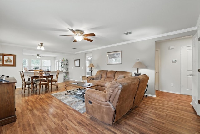 living area with visible vents, ornamental molding, ceiling fan, and wood finished floors
