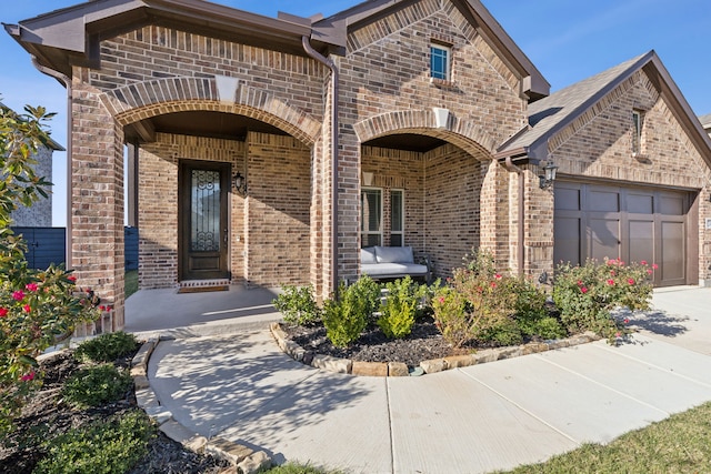 entrance to property with brick siding, an attached garage, and driveway