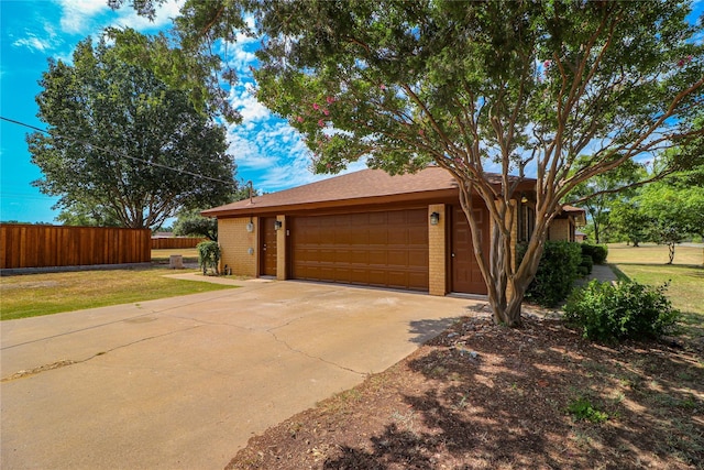 exterior space featuring an attached garage, a yard, fence, brick siding, and driveway