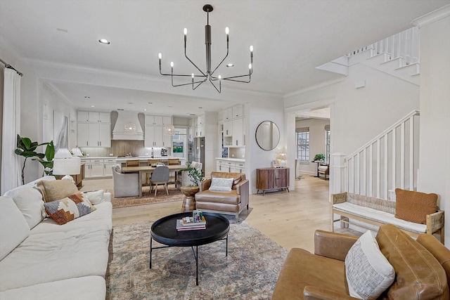 living room with crown molding, an inviting chandelier, light wood-style floors, stairway, and recessed lighting