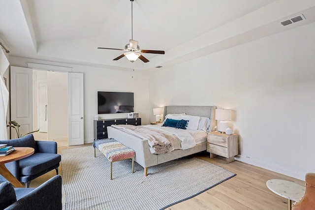 bedroom featuring a raised ceiling, light wood-style floors, a ceiling fan, baseboards, and visible vents