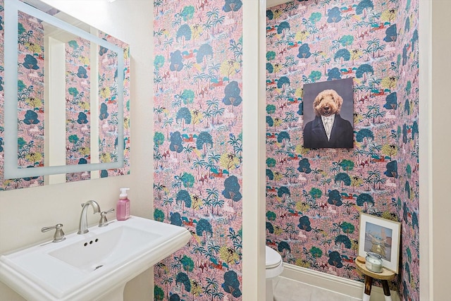 half bathroom with toilet, baseboards, a sink, and tile patterned flooring