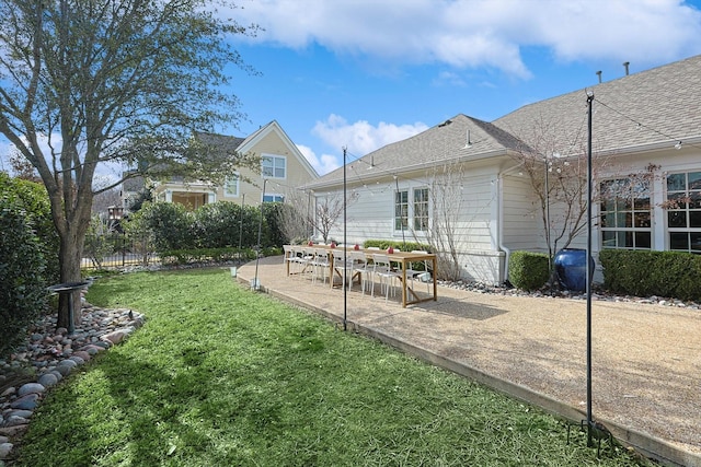 back of property with a lawn, fence, a shingled roof, and a patio area