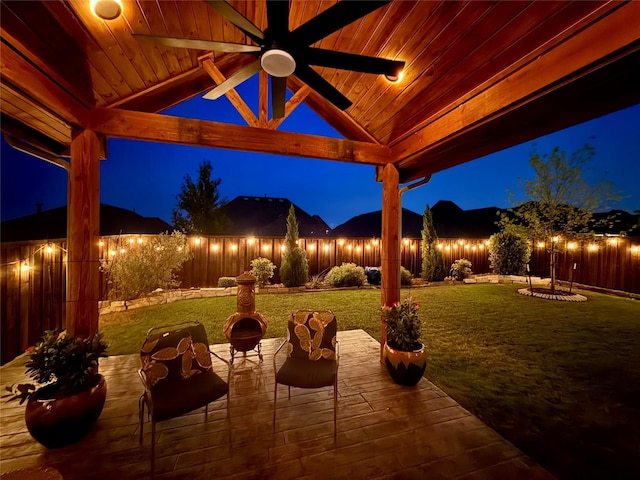 patio at night with a gazebo, a fenced backyard, ceiling fan, and a lawn