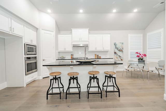 kitchen with stainless steel appliances, a breakfast bar, white cabinetry, and lofted ceiling