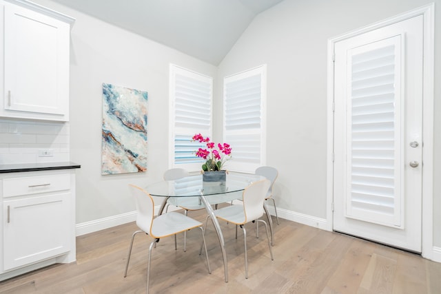 dining space featuring baseboards, light wood finished floors, and vaulted ceiling